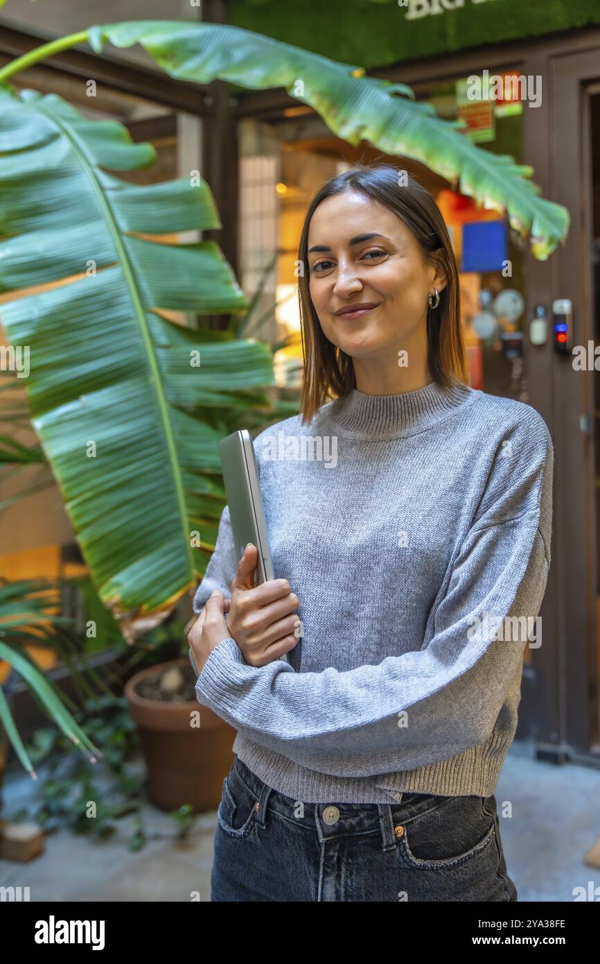 Vertical portrait of a beauty young female entrepreneur standing outside a coworking office holding a laptop Stock Photo