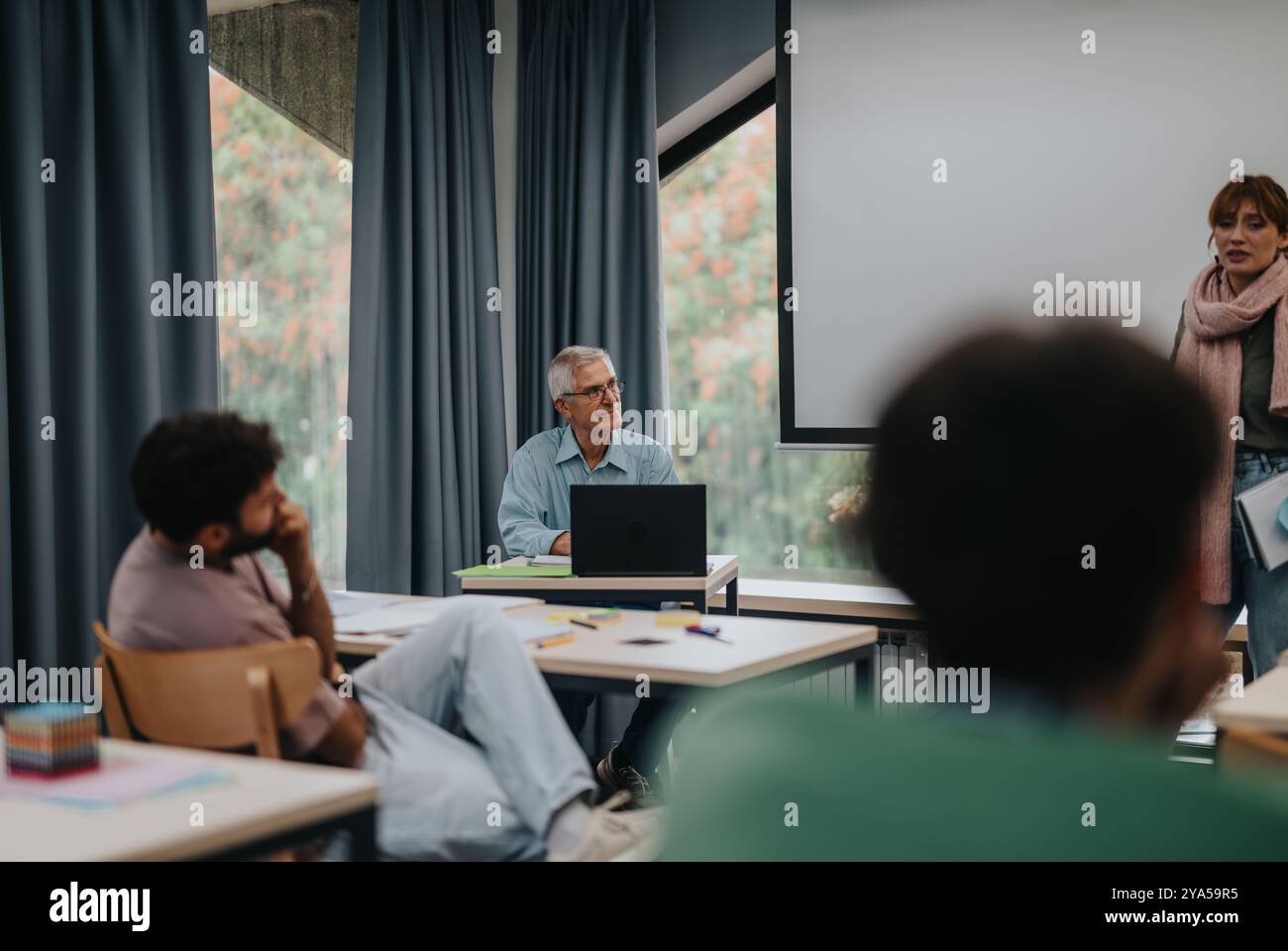 Elderly professor engaging with students in a classroom setting Stock Photo