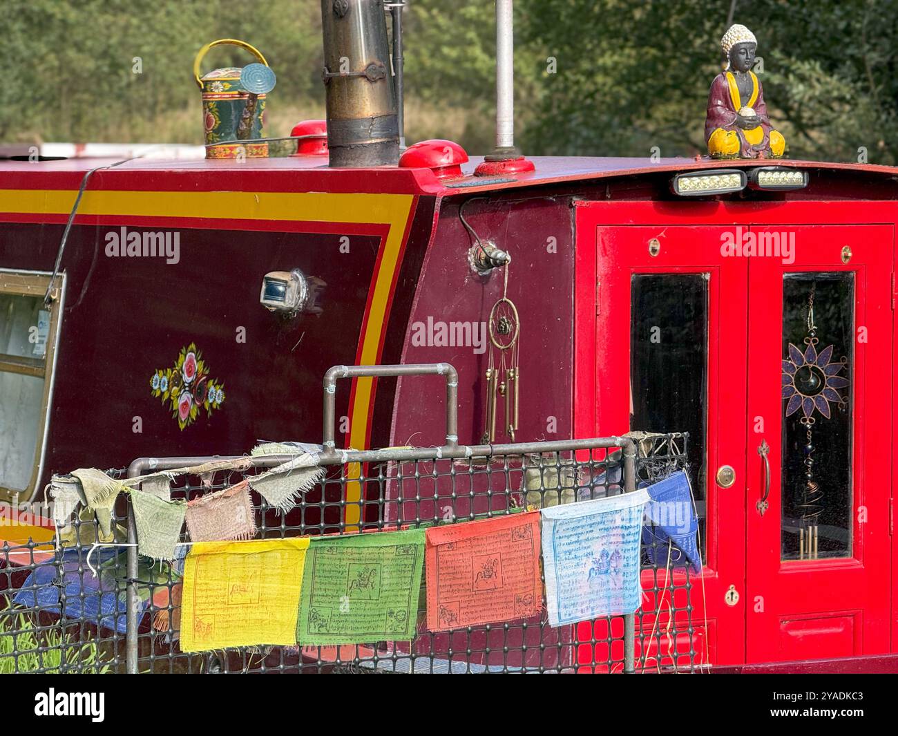Red narrow boat with prayer flags and Buddha statue on Leeds and Liverpool canal at Adlington near Chorley in Lancashire - Smartphone Captured Stock Image