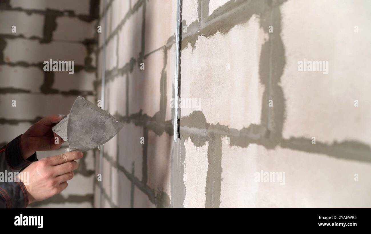 Construction worker applying plaster on white brick wall using trowel. Stock Photo