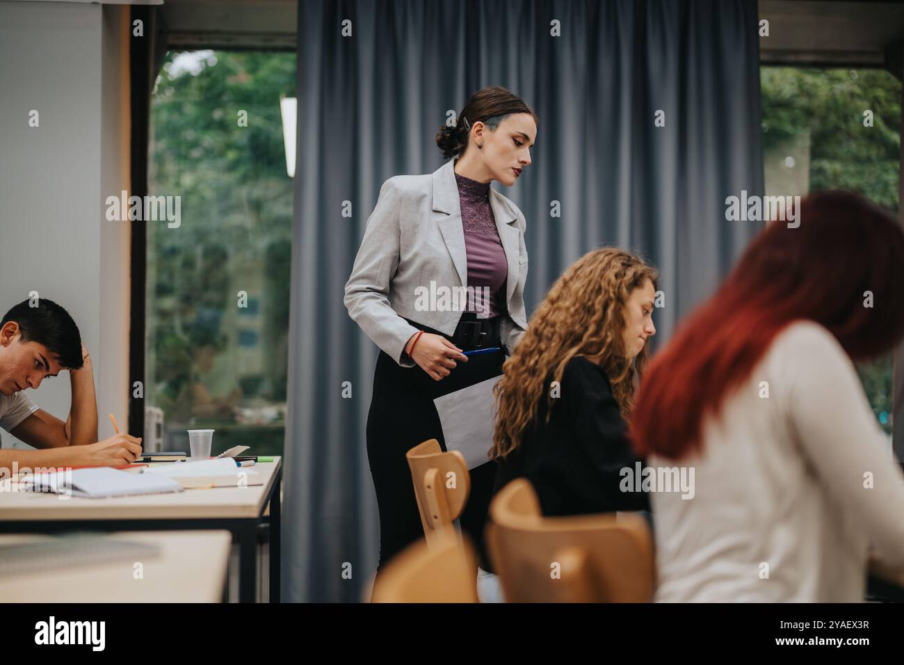 Teacher assisting students during classroom test in modern setting Stock Photo