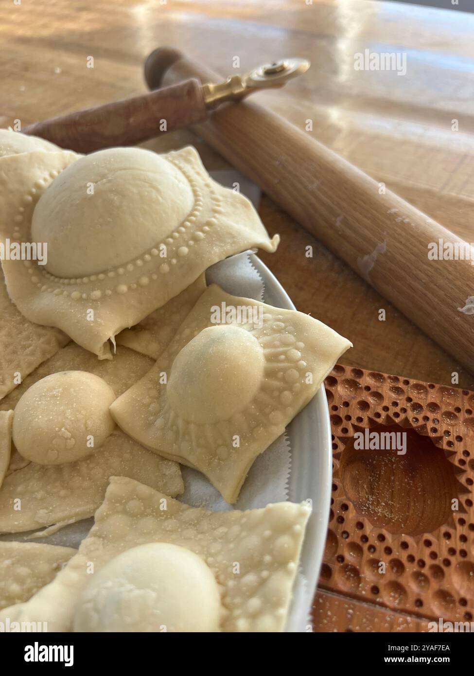 Freshly made ravioli resting on a plate beside a wooden rolling pin and ravioli cutter, ready for the next step in the pasta-making process - Smartphone Captured Stock Image