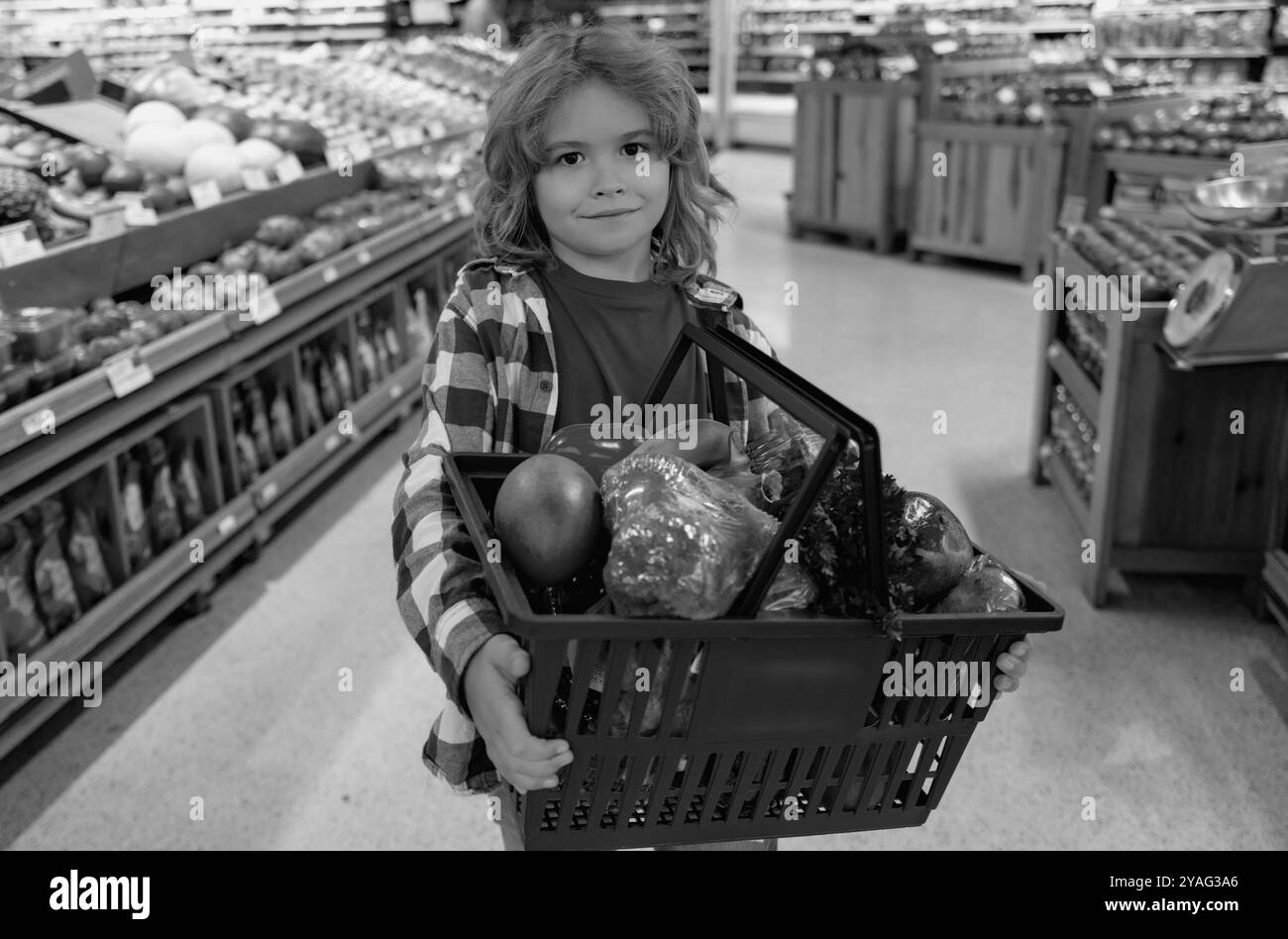 Portrait of child with shopping cart full of fresh vegetables in a food store. Supermarket shopping and grocery shop concept. Shopping kids. Child Stock Photo