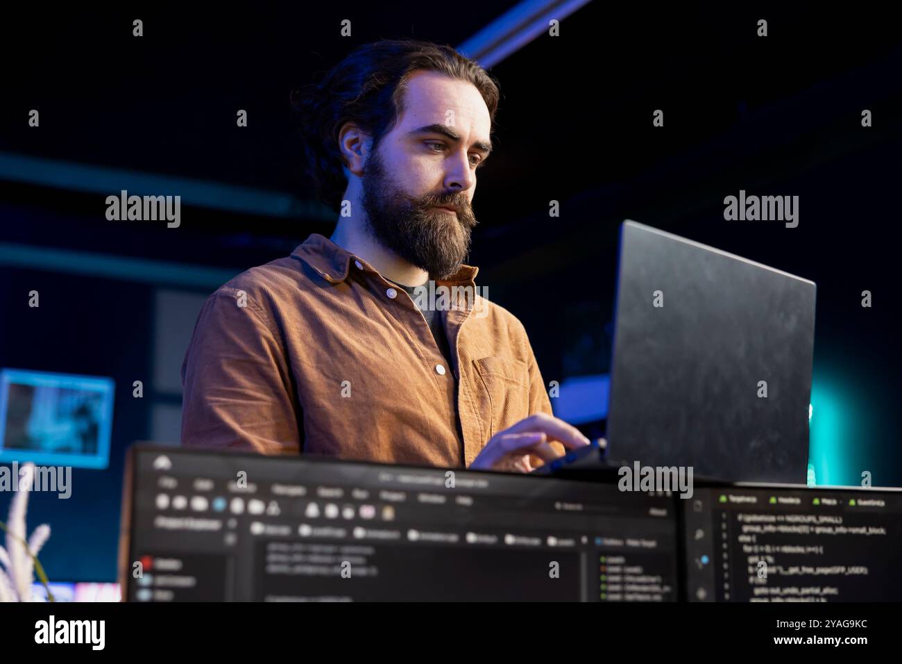 Computer scientist doing software debugging using laptop, checking glitches in lines of code displayed on PC monitors. IT specialist walking around home fixing coding issues using notebook Stock Photo