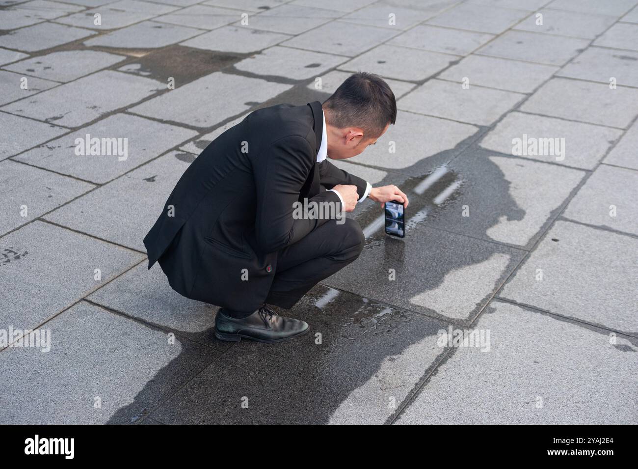 05.04.2019, Singapore, , Singapur - A man squats down in Marina Bay and takes a picture of a reflection in a small puddle with his mobile phone. 0SL19 Stock Photo