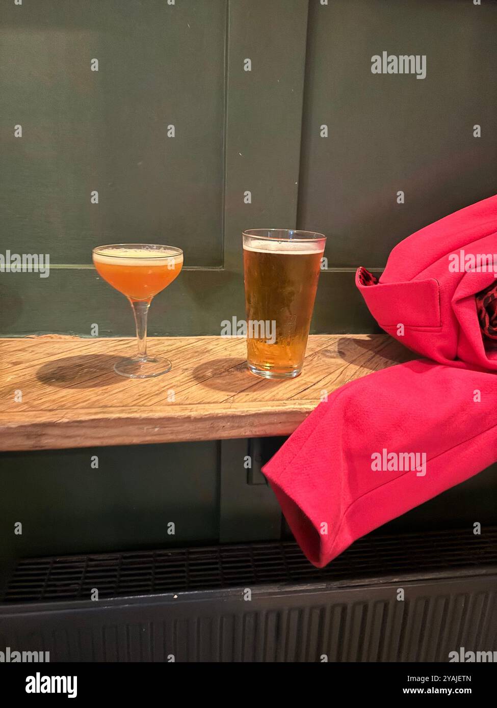 two drinks in a bar - one pint of cider and one orange cocktail next to a coat - Smartphone Captured Stock Image