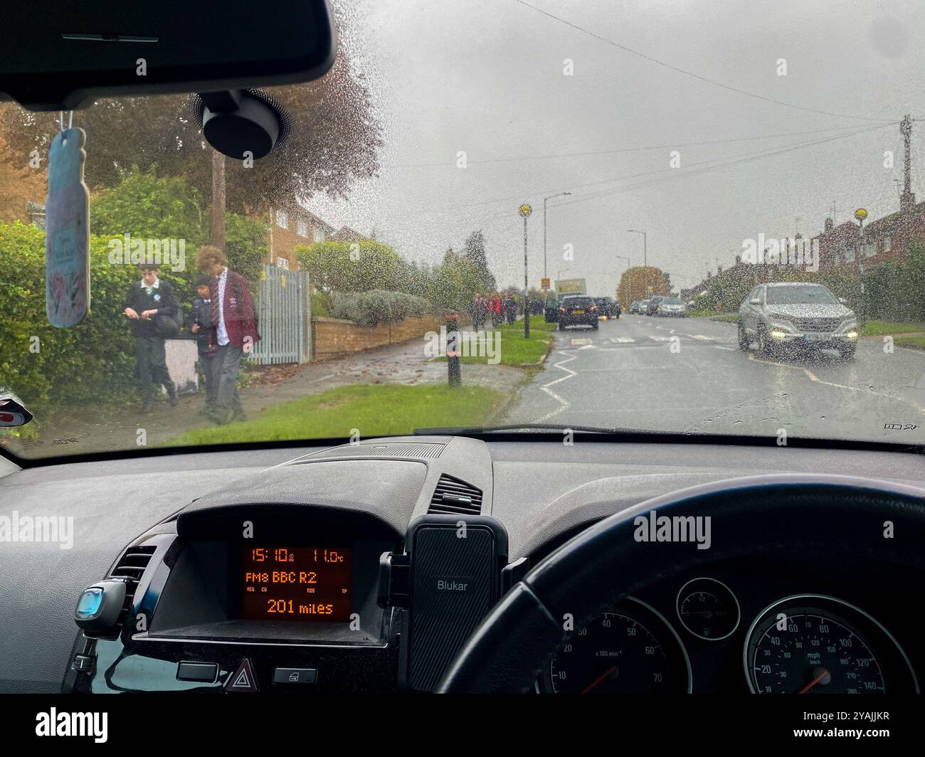 View looking forward from a parked car waiting to pick children up from school at the end of the school day on a wet day in October in Reading, UK - Smartphone Captured Stock Image