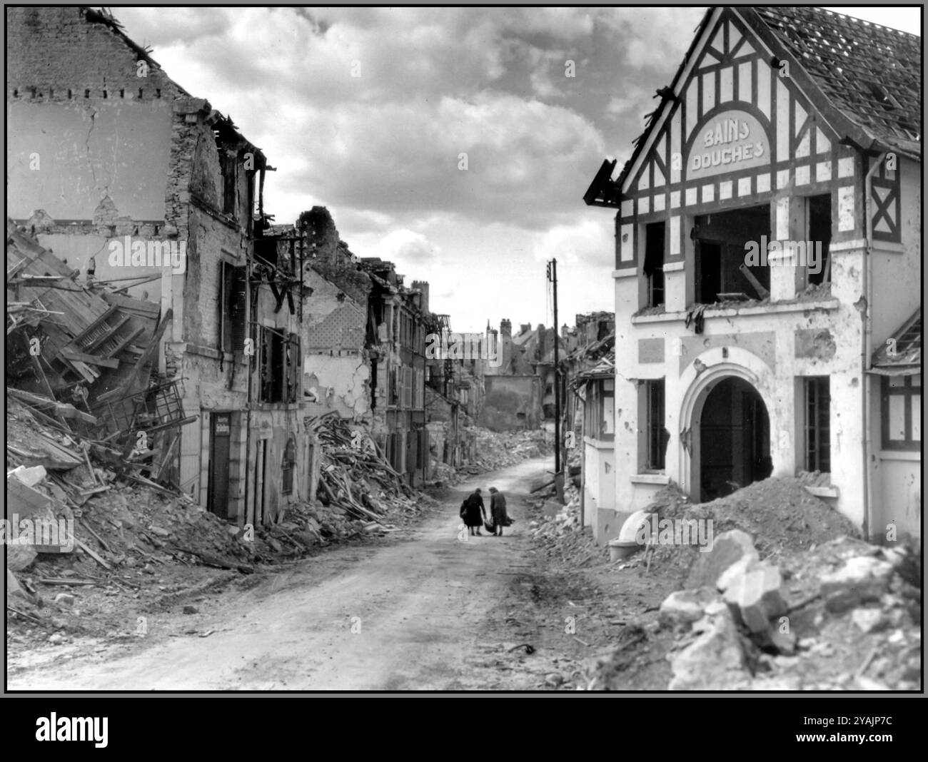 BATTLE OF NORMANDY LIBERATION Two women cross the ruined city. They carry their meager possessions. In the foreground, the remains of the Bains Douches on rue Paul-Doumer Falaise, the impact of the Battle of Normandy on Falaise. Normandy France Stock Photo
