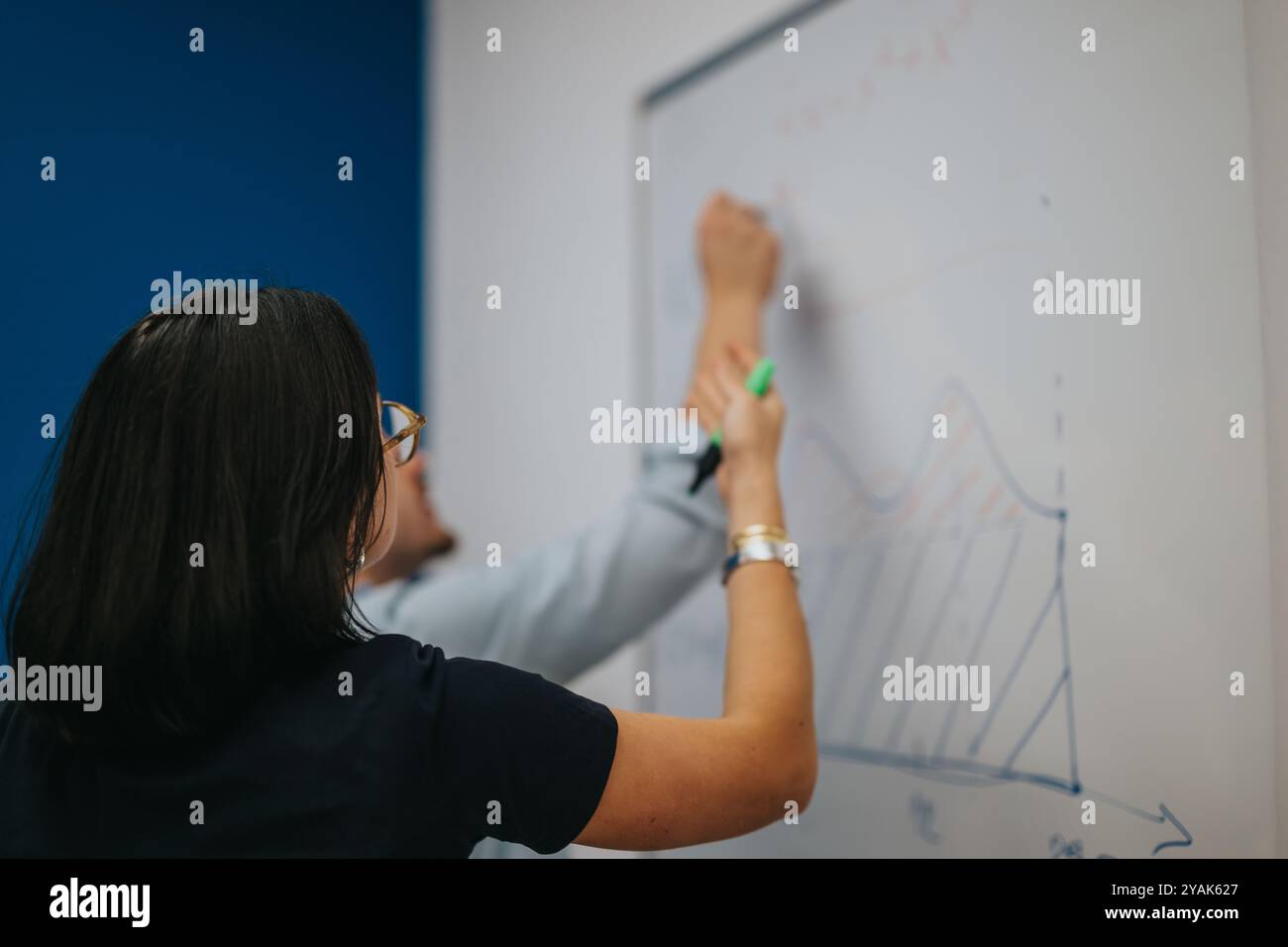 Two people collaborating on a whiteboard with diagrams and data Stock Photo