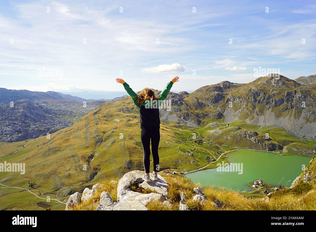 A girl stands with her arms outstretched on top of a cliff against a ...