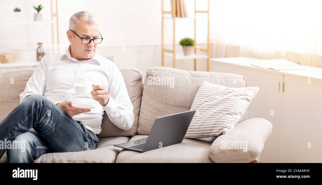 Elderly Man Using Laptop Computer And Having Coffee Stock Photo