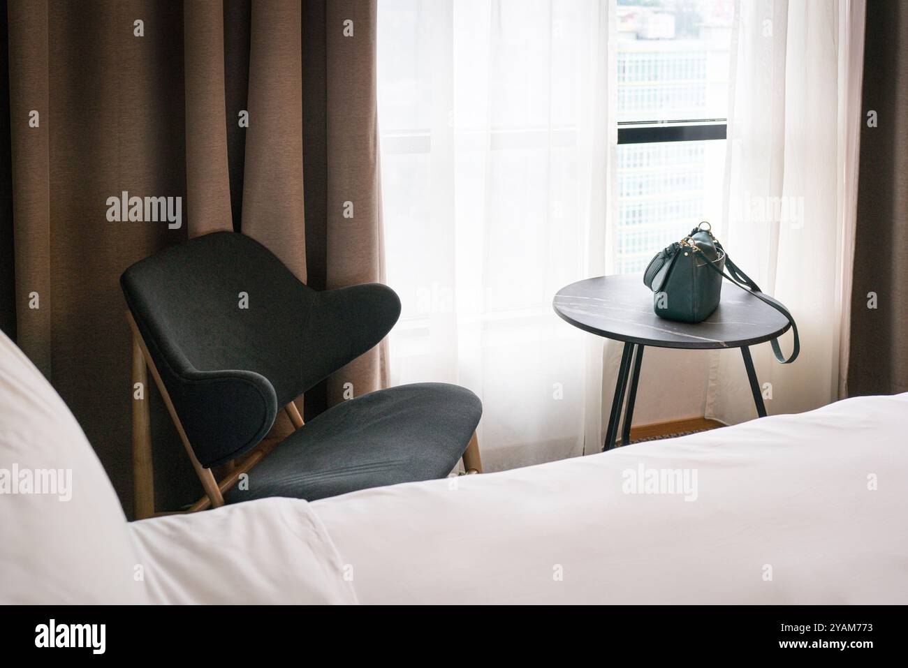 Hotel room with bed covered with white blanket, chair and table. Stock Photo