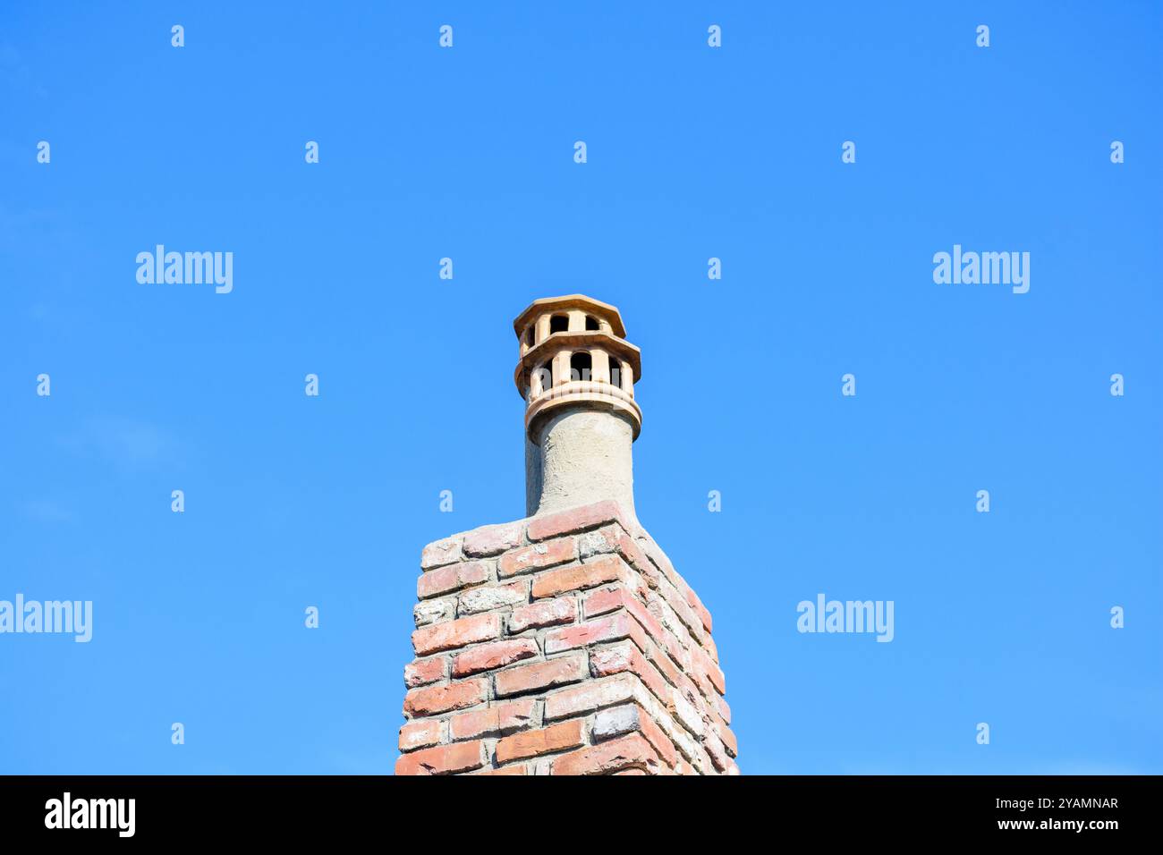 A brick chimney topped with two ornately designed clay chimney pots, set against a clear sky. Stock Photo
