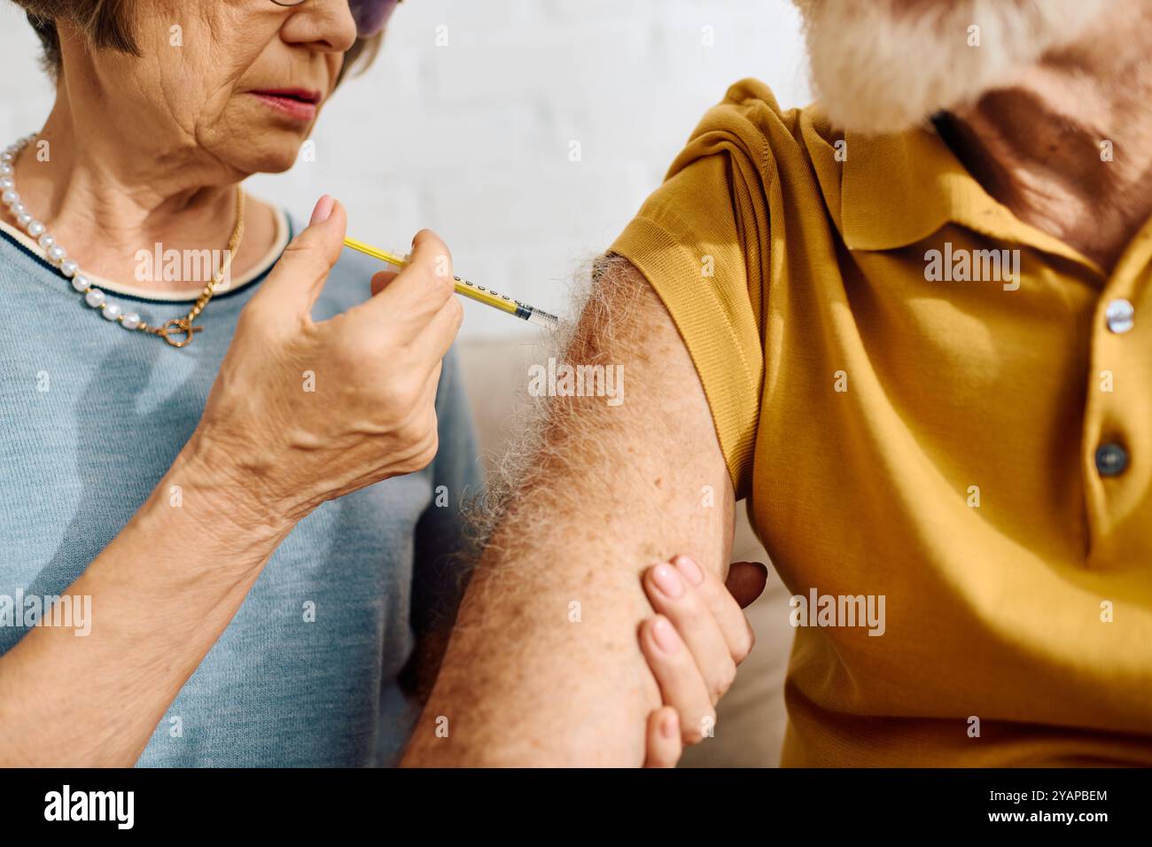 A devoted wife gently provides insulin to her diabetic husband in their cozy living room. Stock Photo