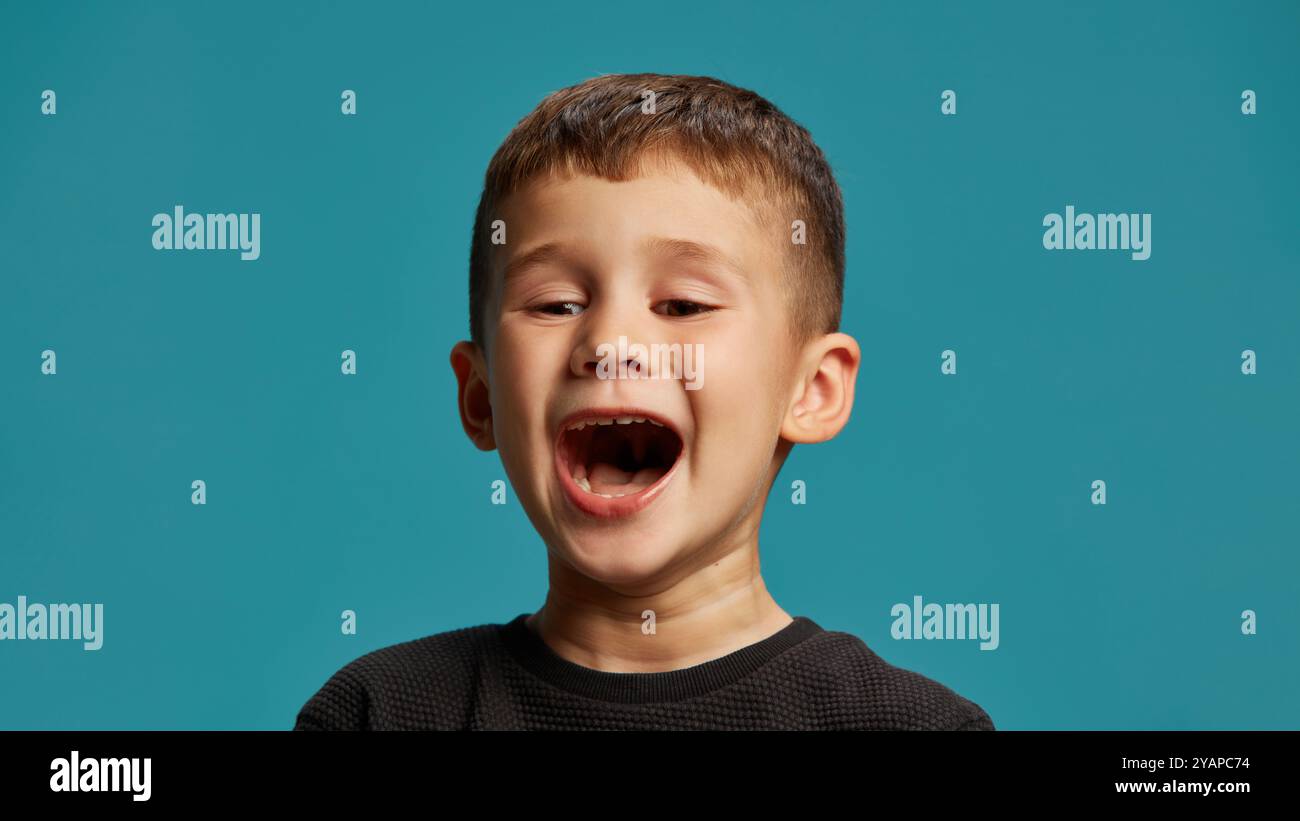 Boy opens his mouth wide, as if shouting or singing with all energy ...