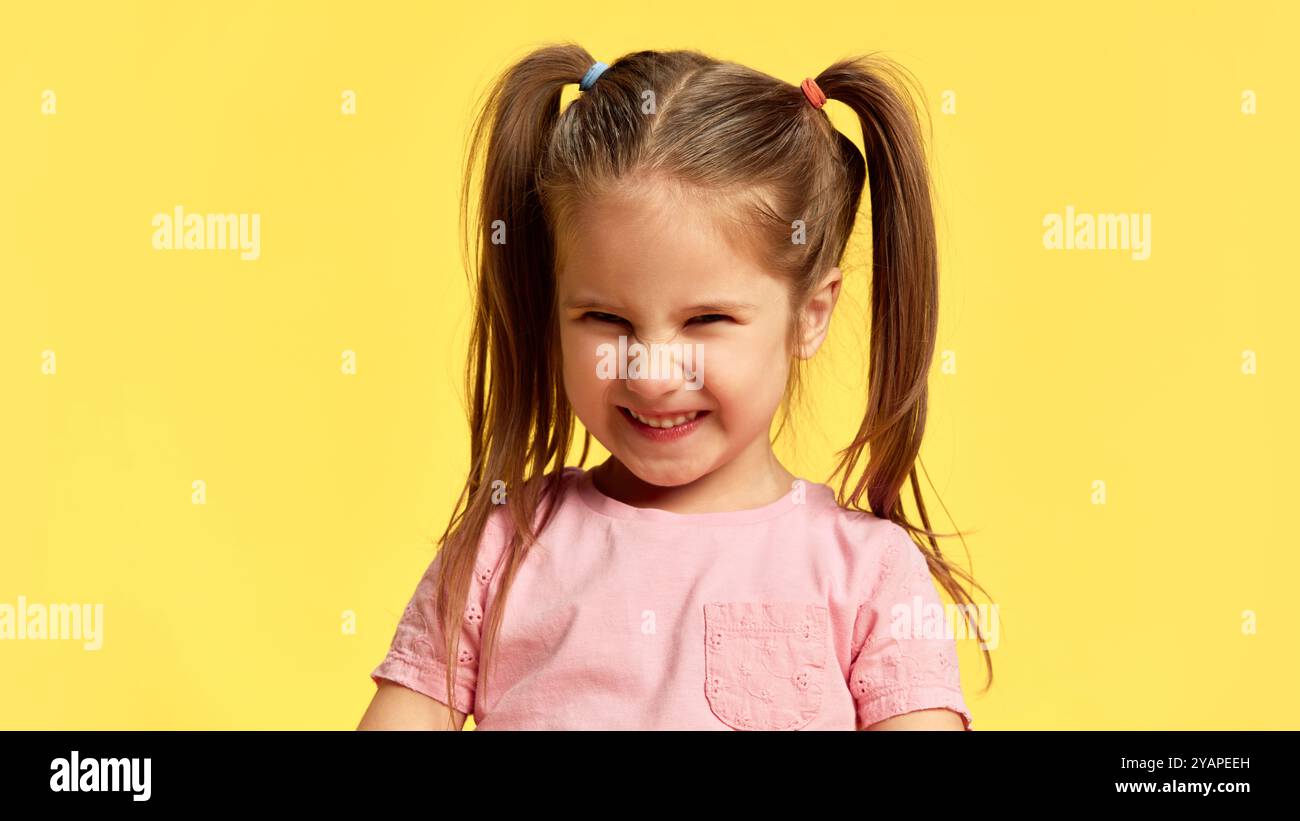 Portrait of girl closes her eyes, smiling with scrunched-up face in pure joy against sunny ...