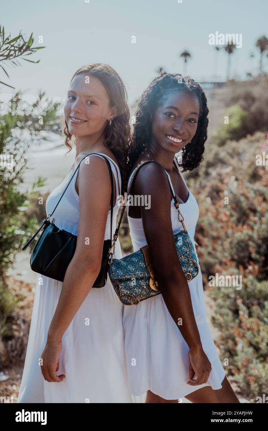 Two friends are standing back to back, both wearing white dresses, diversity concept. Stock Photo