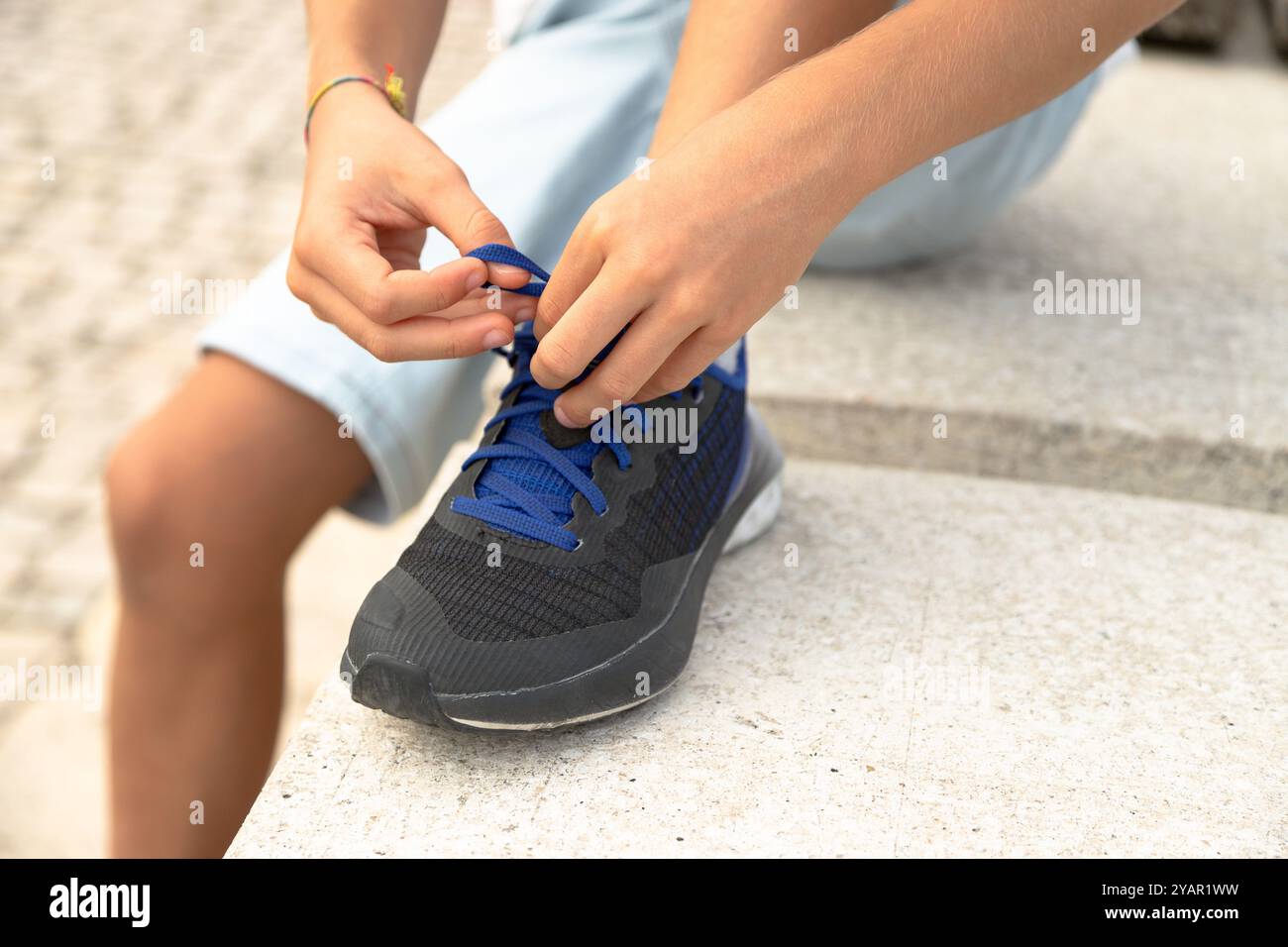 Detail of a child sitting trying to tie his shoelaces with laces ...