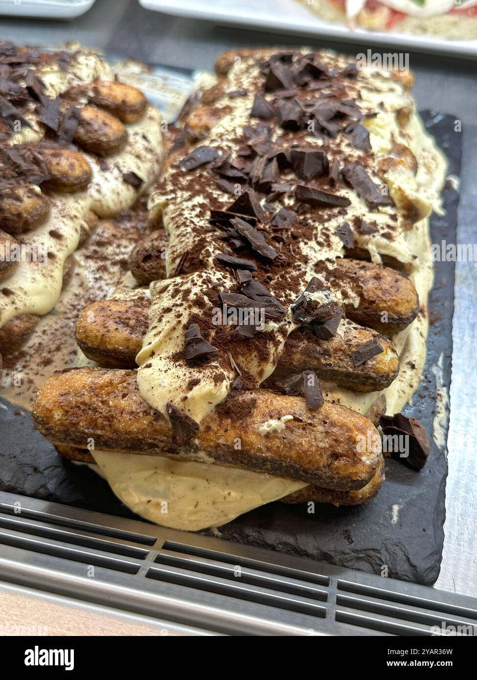 Tiramisu, featuring lady fingers cookies and topped with chocolate crumbles, is shown on display in an artisan dessert shop in Italy. - Smartphone Captured Stock Image