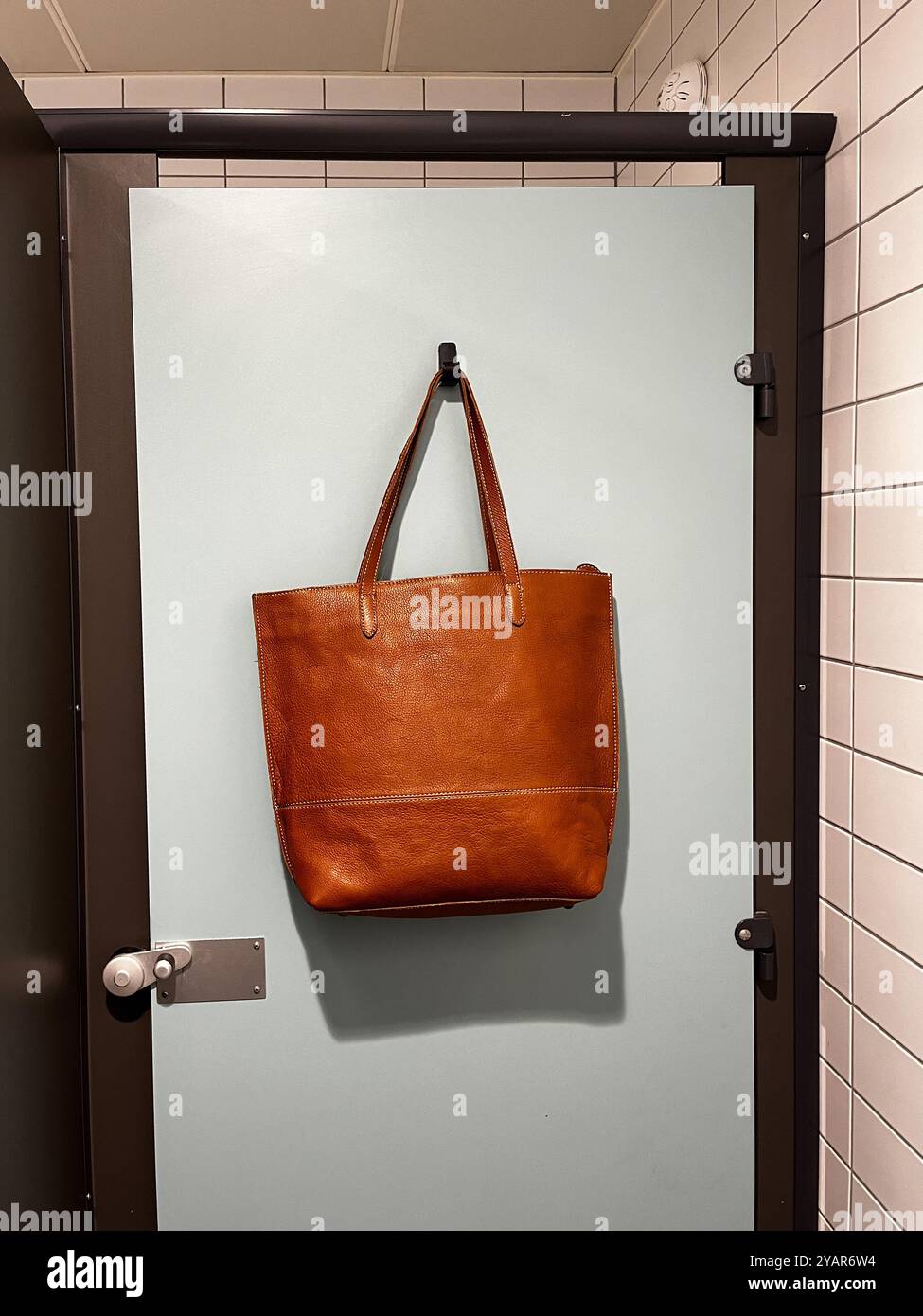 Brown Leather Tote Shopping Bag Hanging On The Back of A Public Toilet Door - Smartphone Captured Stock Image
