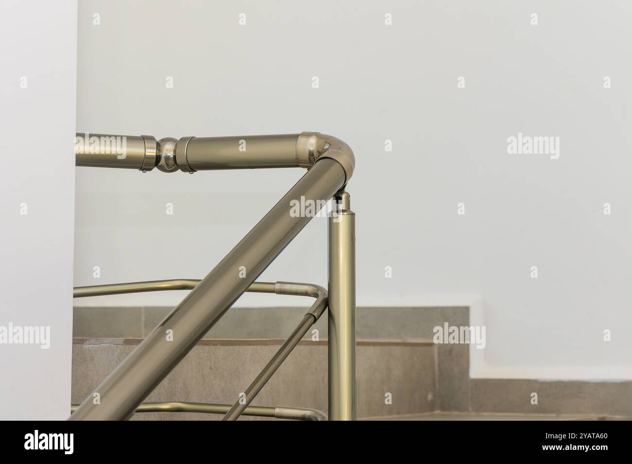 The sleek metal railing curves elegantly, showcasing its modern design against the crisp white wall and gray steps, creating a striking visual contras Stock Photo