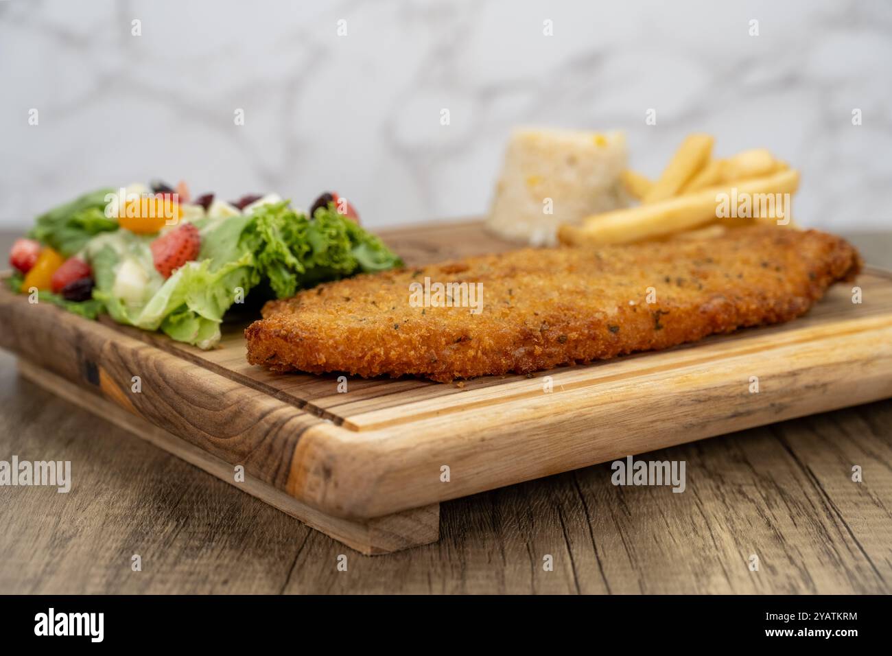 Breaded fish fillet arranged on a wooden platter and served with french fries and salad for a delicious seafood meal. Stock Photo