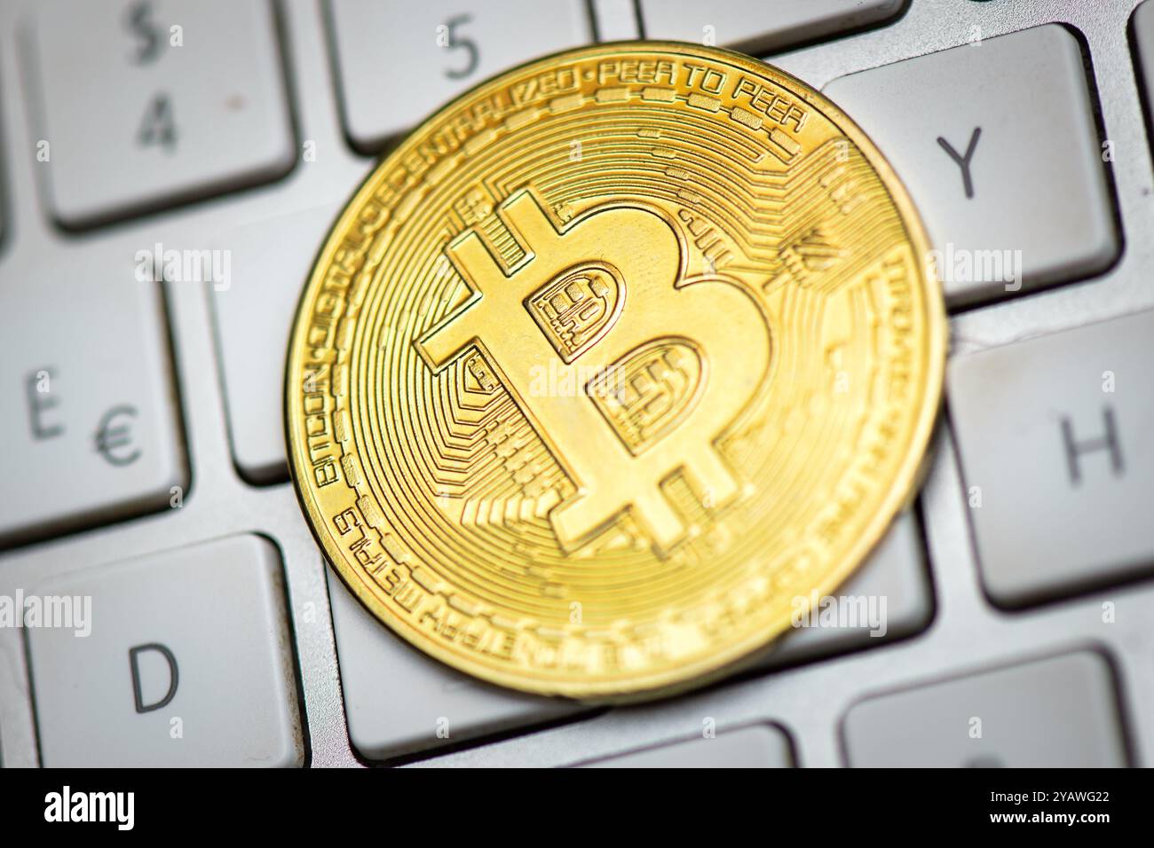 Bitcoin leaning against a computer keyboard on white background Stock Photo