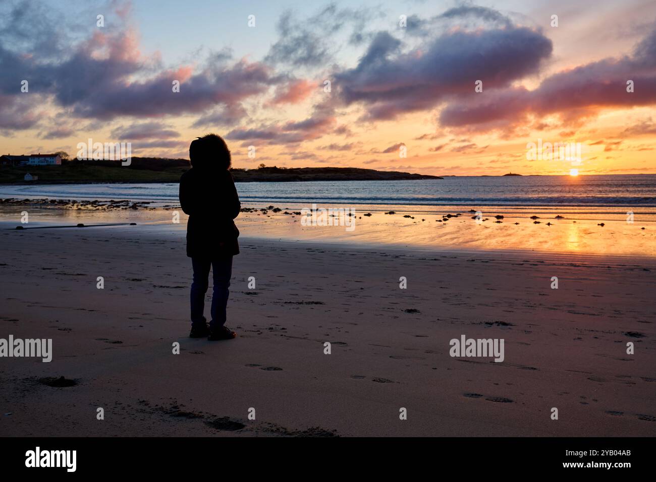 Woman looking at a wintery sunset from the beach Stock Photo