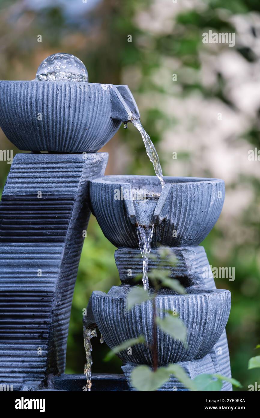 A close-up view of a tiered garden water fountain with three bowls and flowing water. Stock Photo