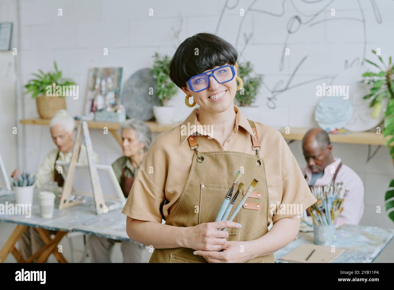 Portrait of young adult Caucasian drawing teacher holding paintbrushes and posing for photo Stock Photo