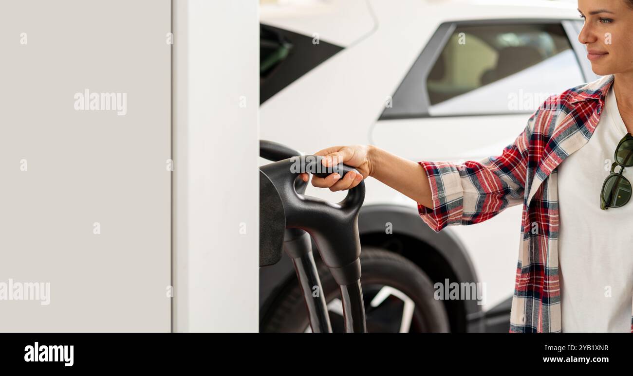 Innovating Electric Mobility. Woman Engaging with EV Charging Station. Female car driver takes electric charge connector. Stock Photo