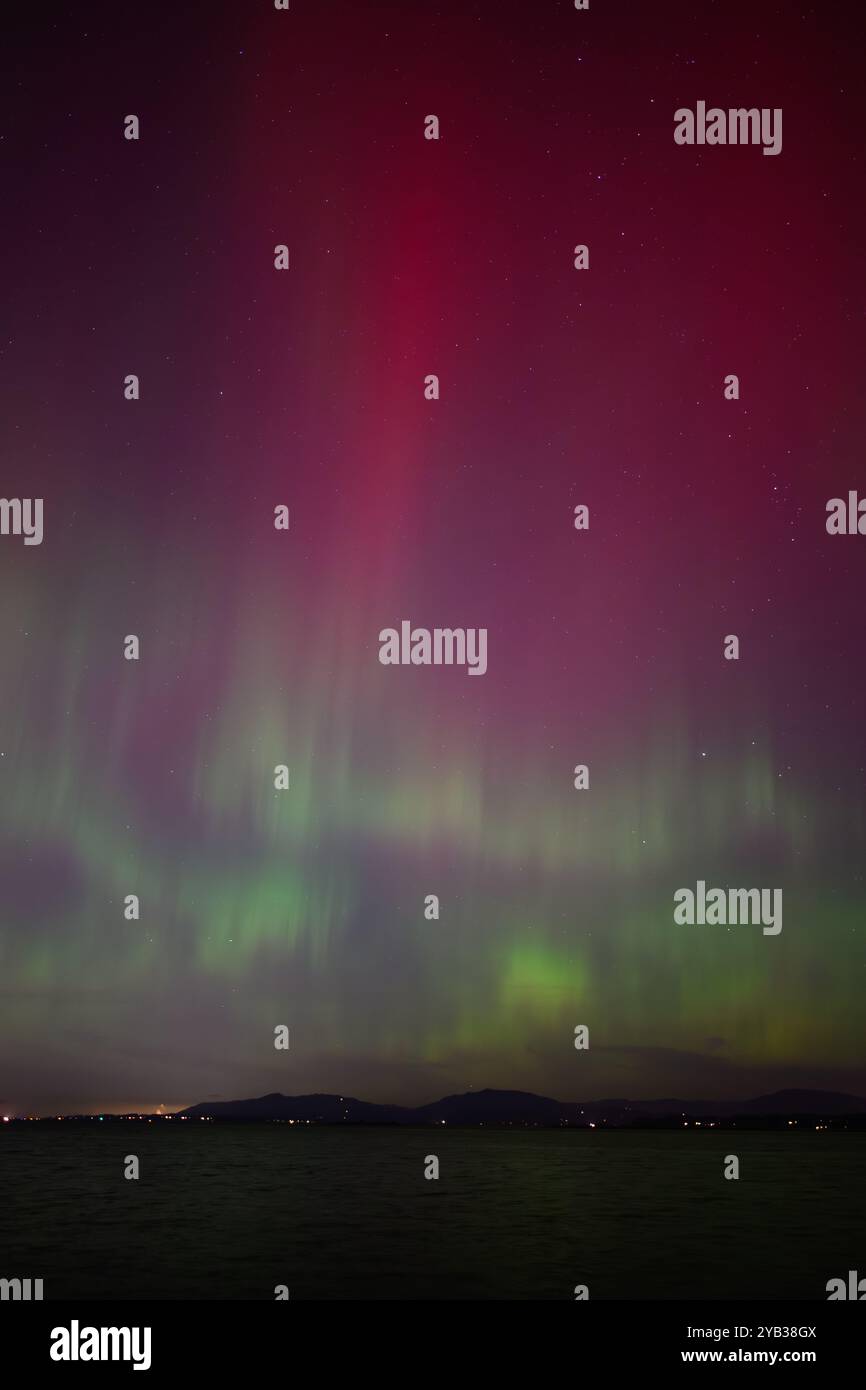 Aurora Borealis Northern Lights with red pillar and green waves over water Stock Photo