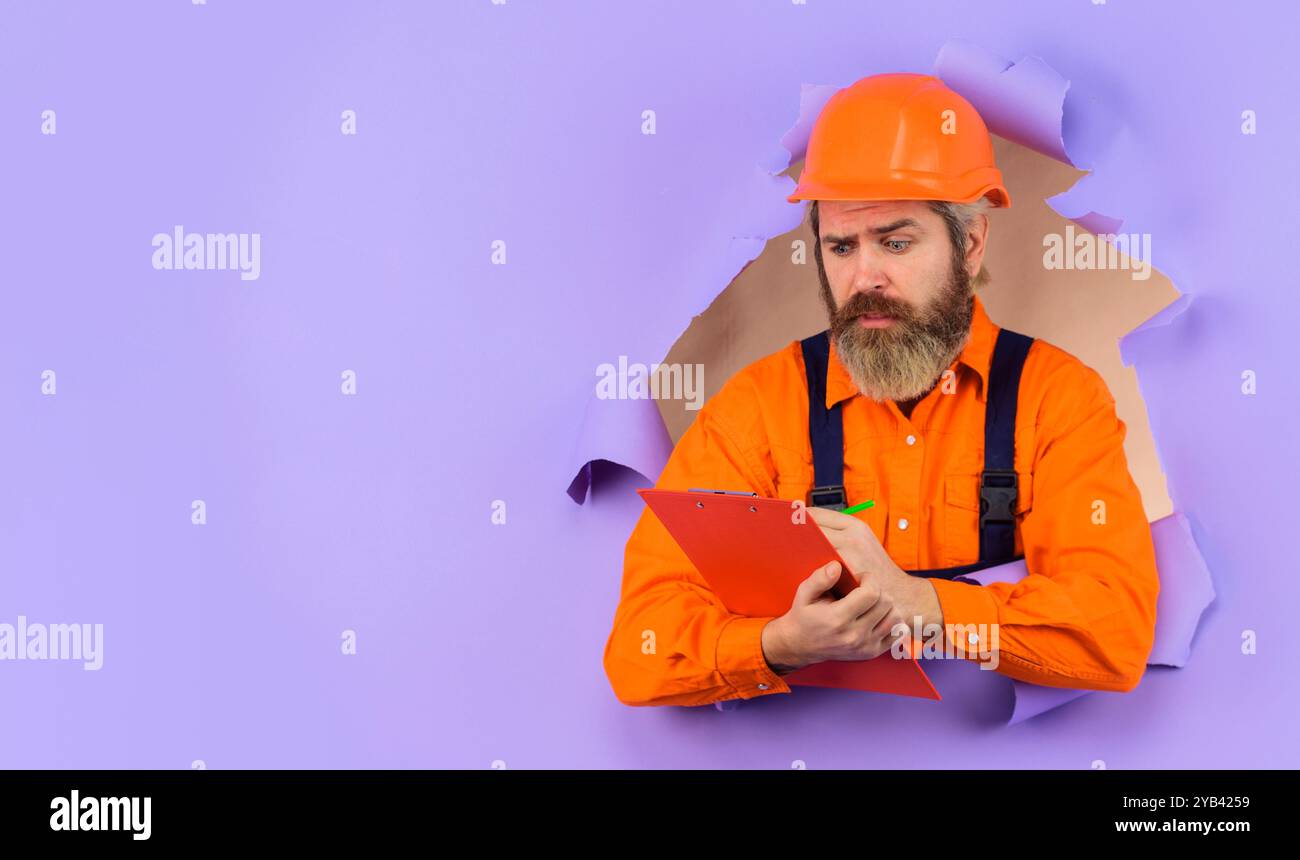 Male builder, architect or inspector in uniform with checklist looking ...