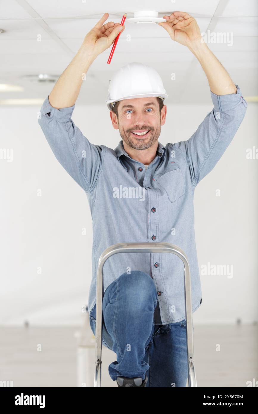 man using screwdriver to install smoke detector on ceiling Stock Photo