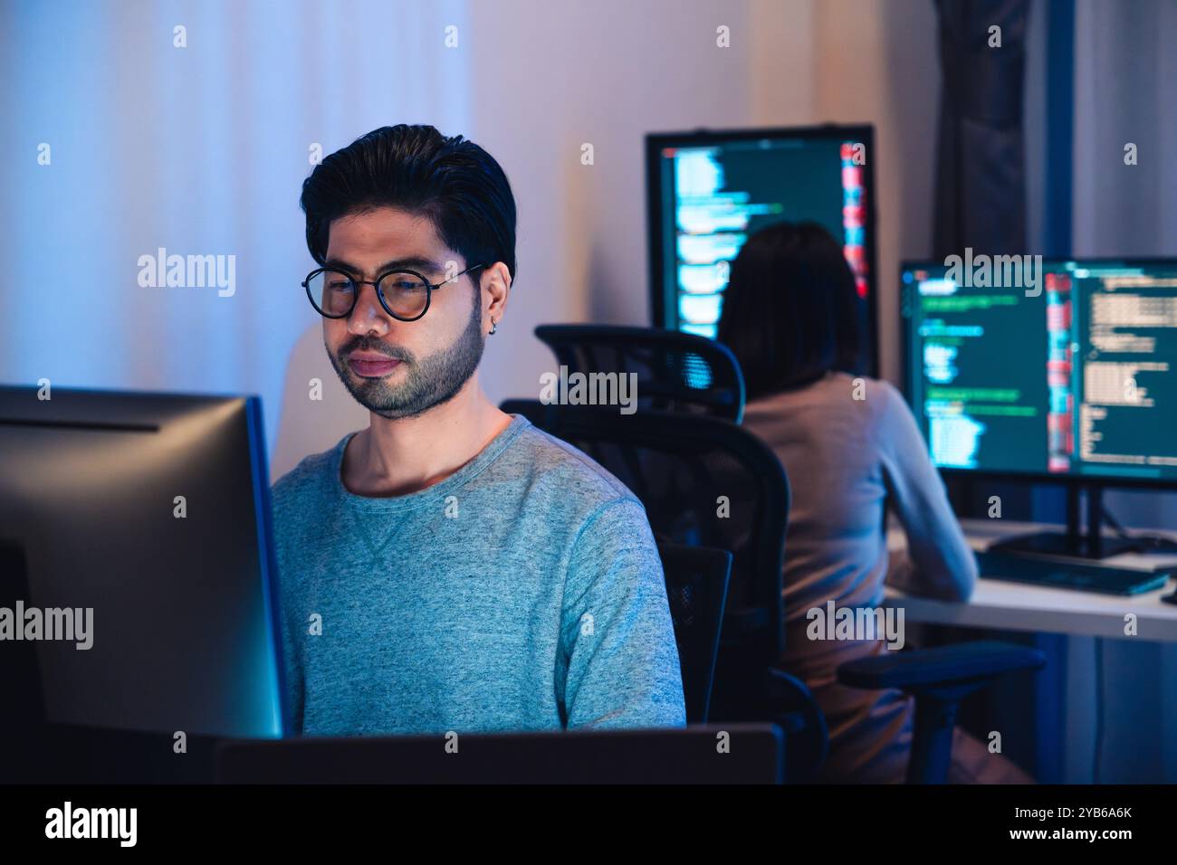 Asian software developers working on multiple screens displaying code and application diagrams at night in modern office Stock Photo