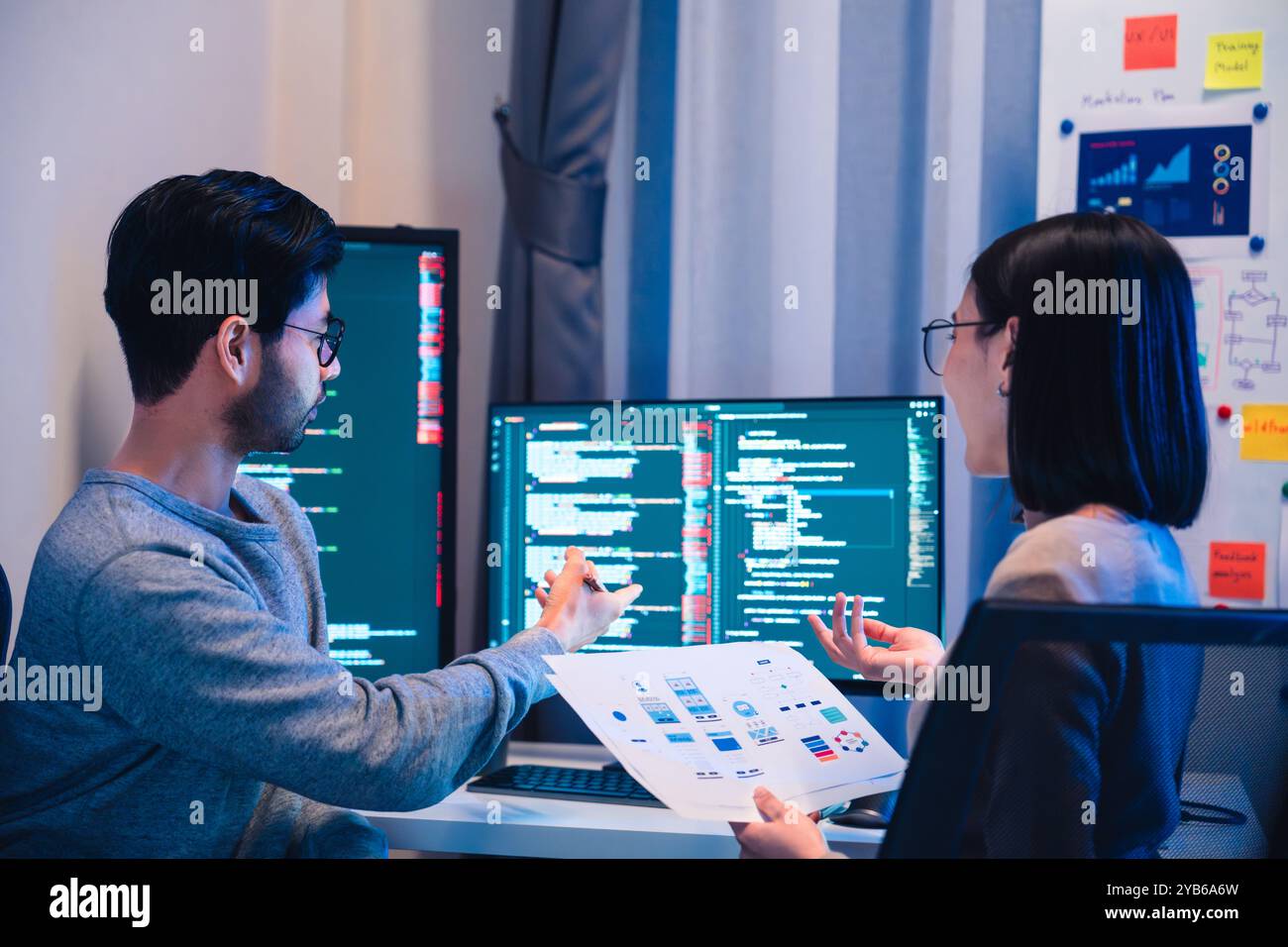 Asian software developers teams working on multiple screens displaying code and application diagrams at night in modern office Stock Photo