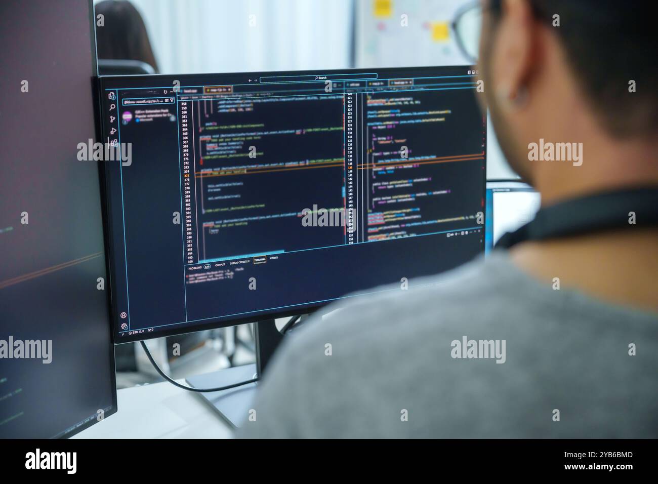 Asian software developers working on multiple screens displaying code and application diagrams in a modern office Stock Photo