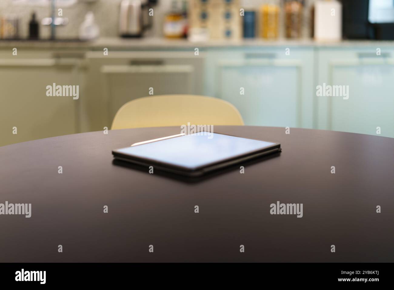 E-reader on kitchen table. Graphic tablet white screen mockup. Home office interior. Stock Photo