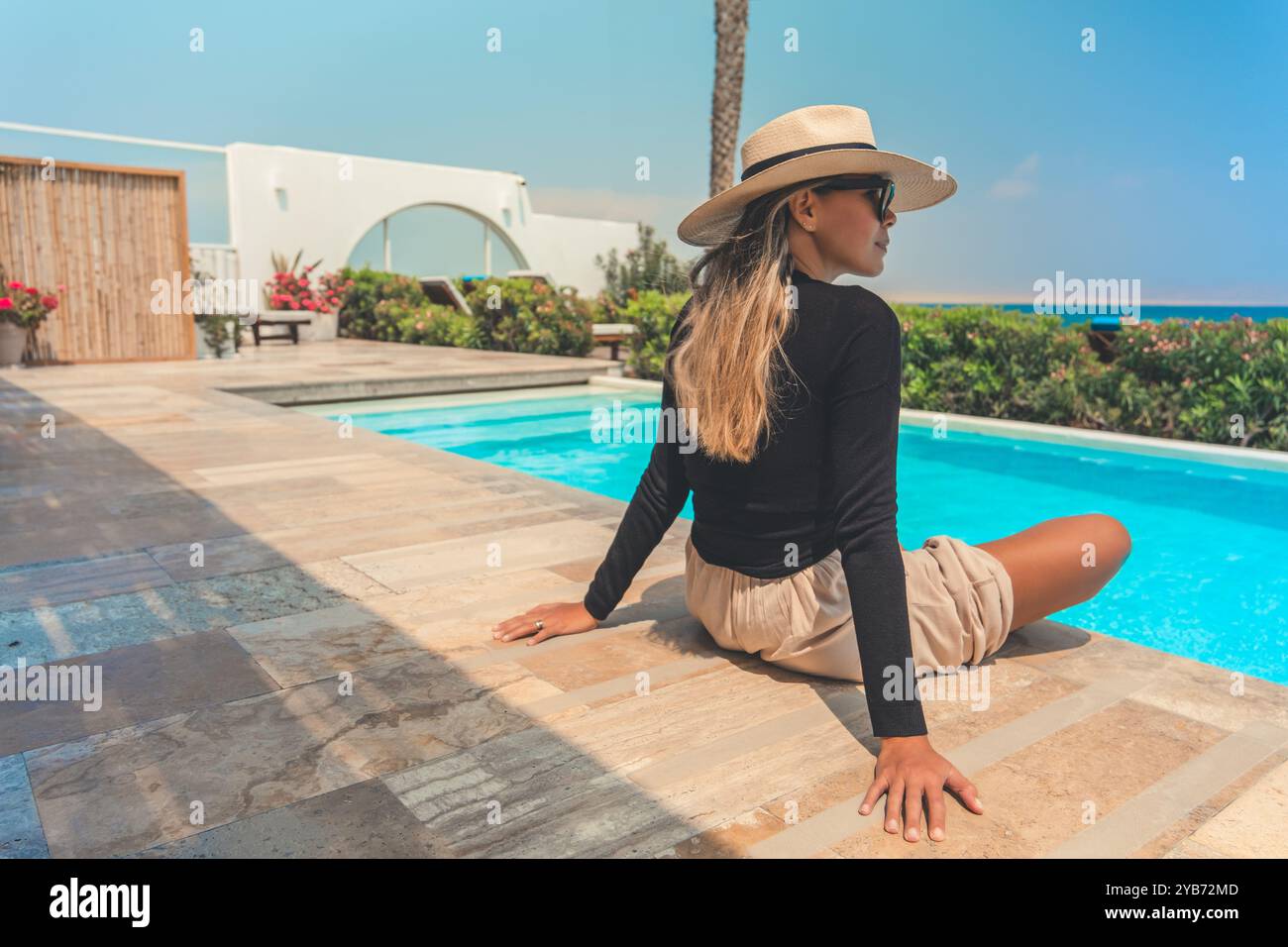 A woman wearing a straw hat is sitting on a pool deck Stock Photo - Alamy