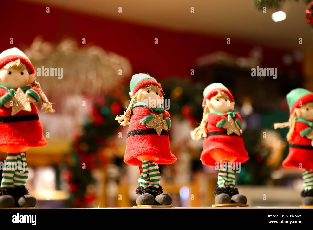 Selective focus on small festive Christmas Elf figurine, holding spruce branch, next to pine cones and tea candle light. Dark evening room with lot of Stock Photo