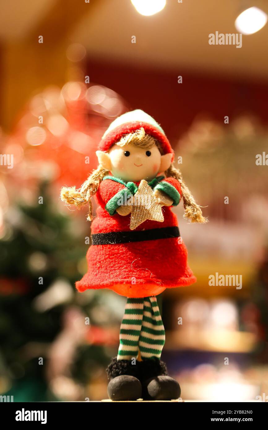 Selective focus on small festive Christmas Elf figurine, holding spruce branch, next to pine cones and tea candle light. Dark evening room with lot of Stock Photo