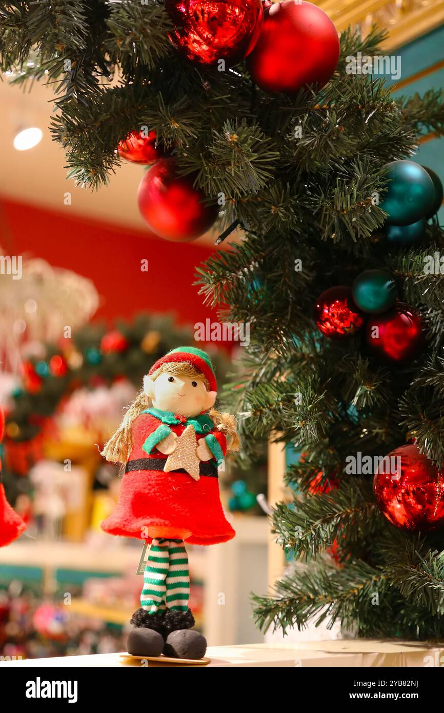 Selective focus on small festive Christmas Elf figurine, holding spruce branch, next to pine cones and tea candle light. Dark evening room with lot of Stock Photo