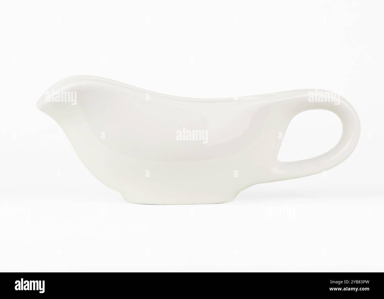 A ceramic gravy boat with a sleek, modern design sits against a plain white background. Ideal for serving sauces and gravies at gatherings and family meals Stock Photo