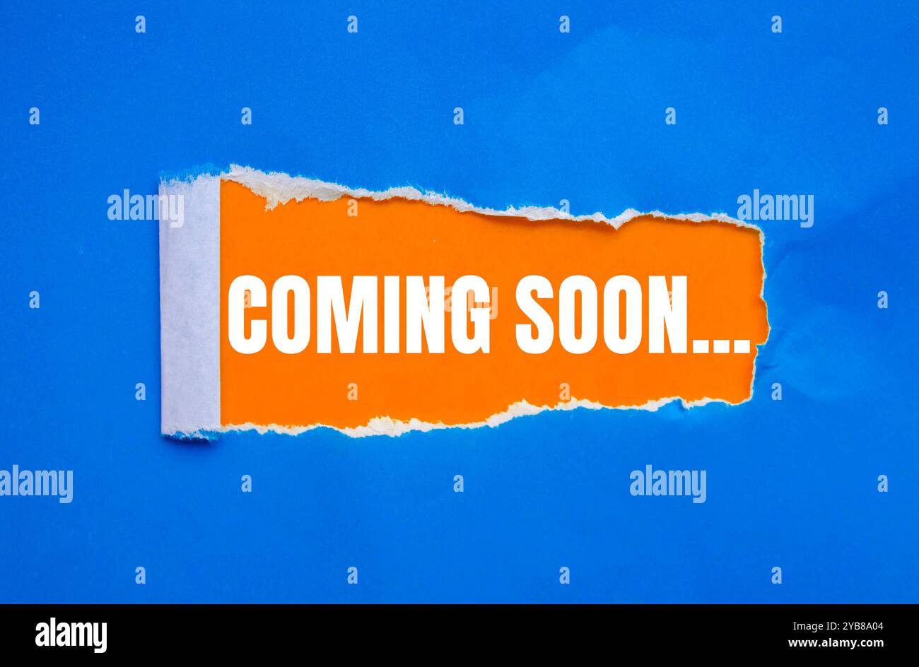 Coming soon message written on ripped torn blue paper with orange ...