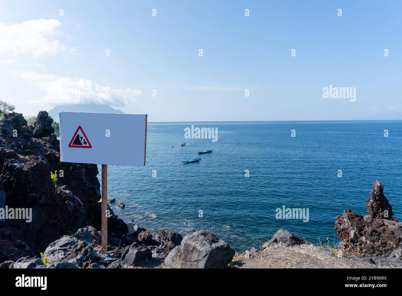 Danger Sign of Falling Rocks on the edge of a cliff with a sea background Stock Photo