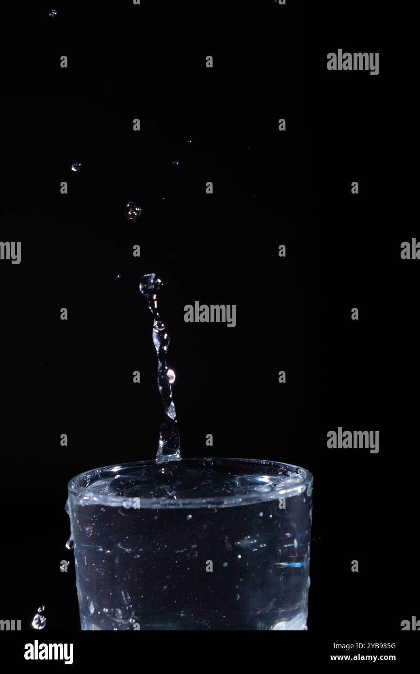 Water erupts dramatically from a glass, creating droplets and splashes ...