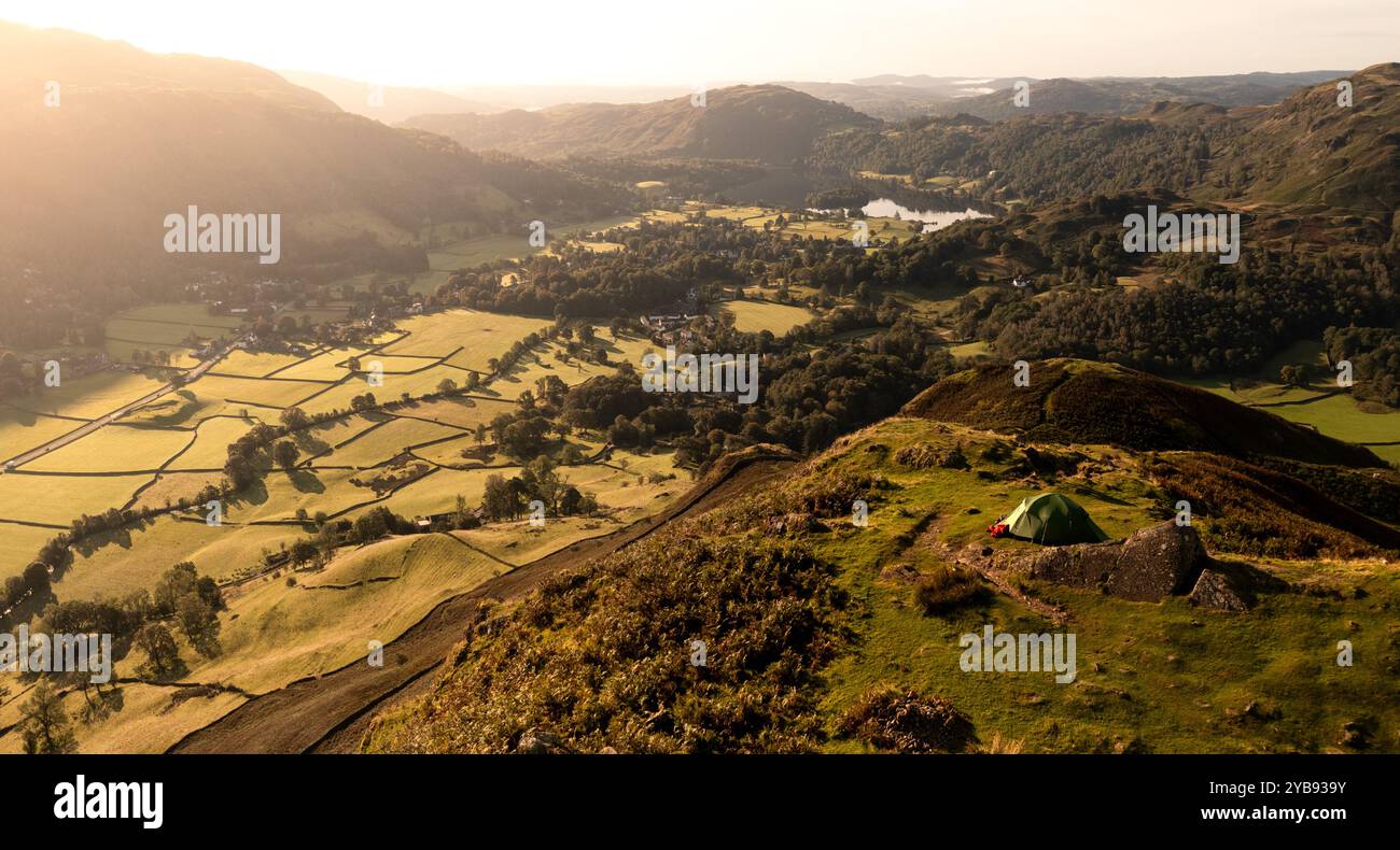 Aerial panoramic landscape of the Lake District village of Grasmere above Grasmere lake with people camping in a tent high on a hillside with a scenic Stock Photo