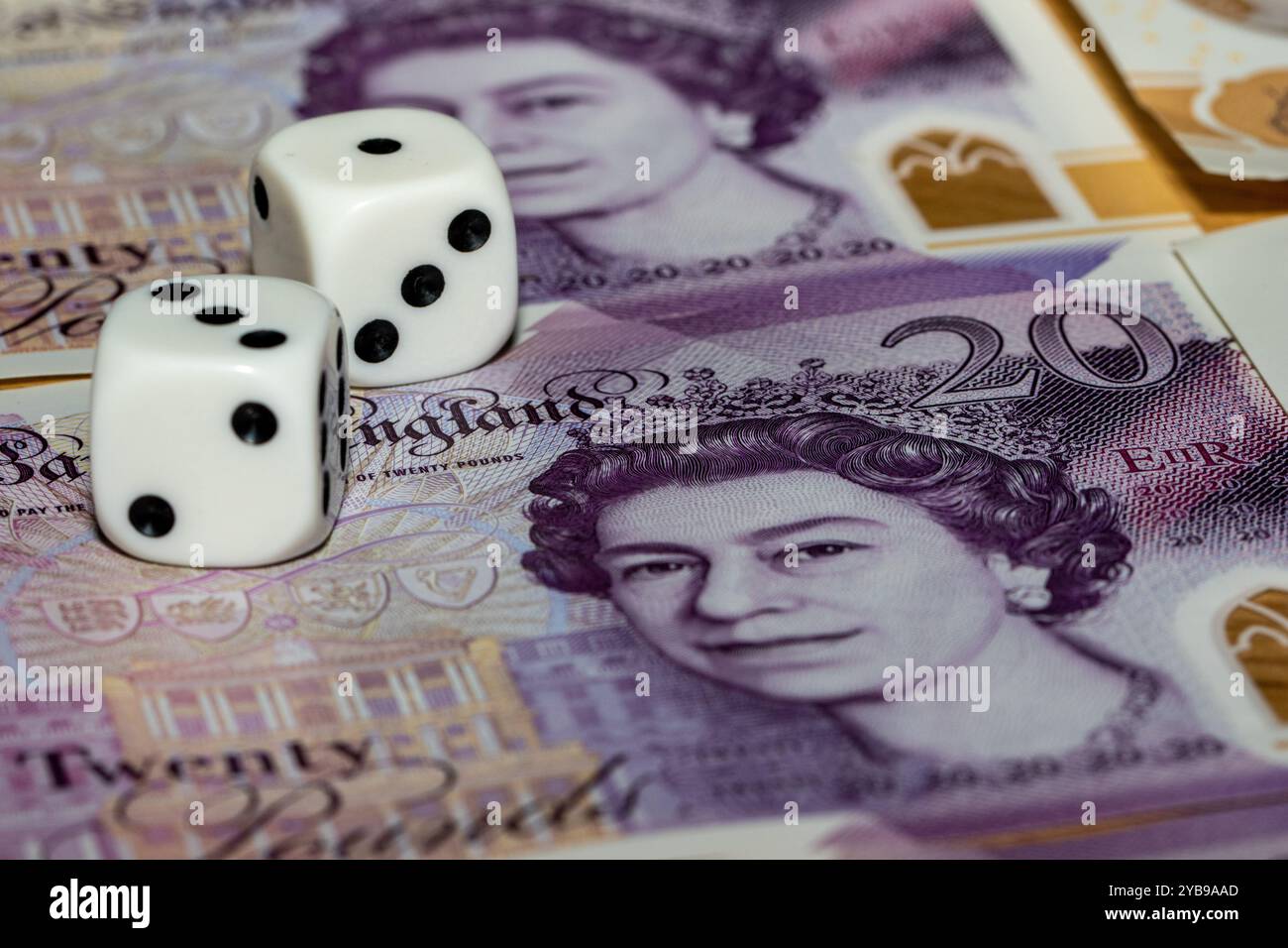 Two white dice with black dots rest on a twenty pound note featuring Queen Elizabeth II. The note is partially visible, showing the denomination and s Stock Photo