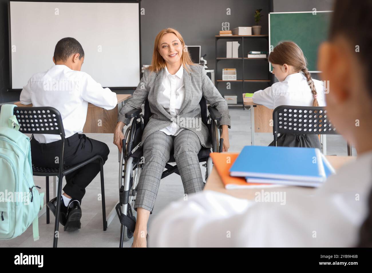 Mature teacher in wheelchair conducting lesson to little pupils at ...