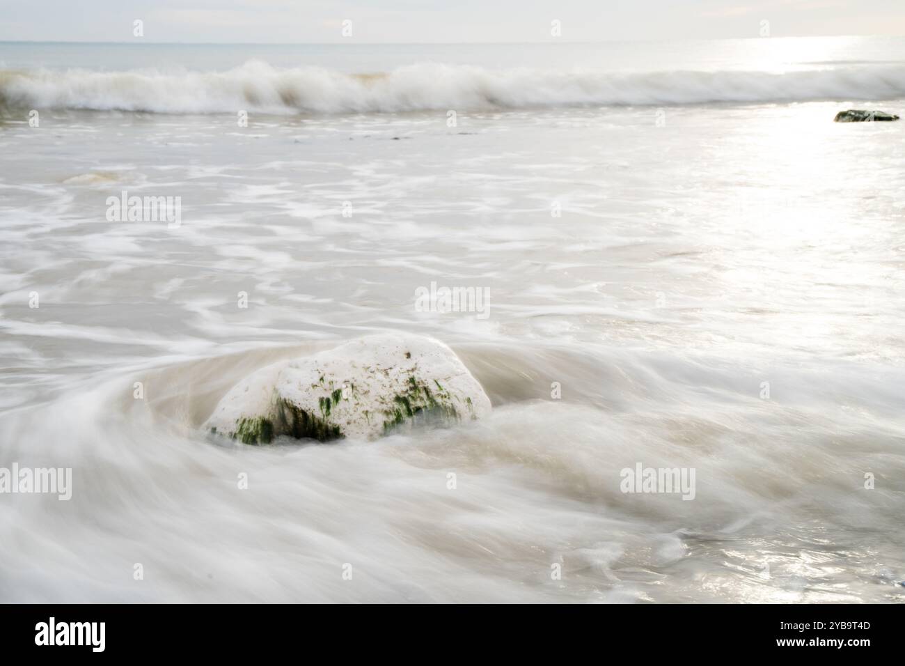 Waves in slow motion crashing onto a stone on a beach England UK Stock Photo